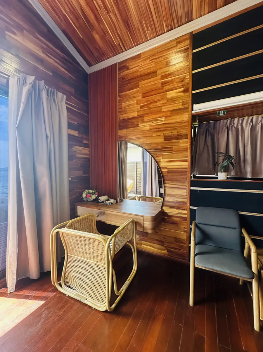 A charming vanity area inside a bedroom at Dayang Resort in the Semporna featuring a modern woven chair, traditional style wood walls with glossy wooden floors, and air con.