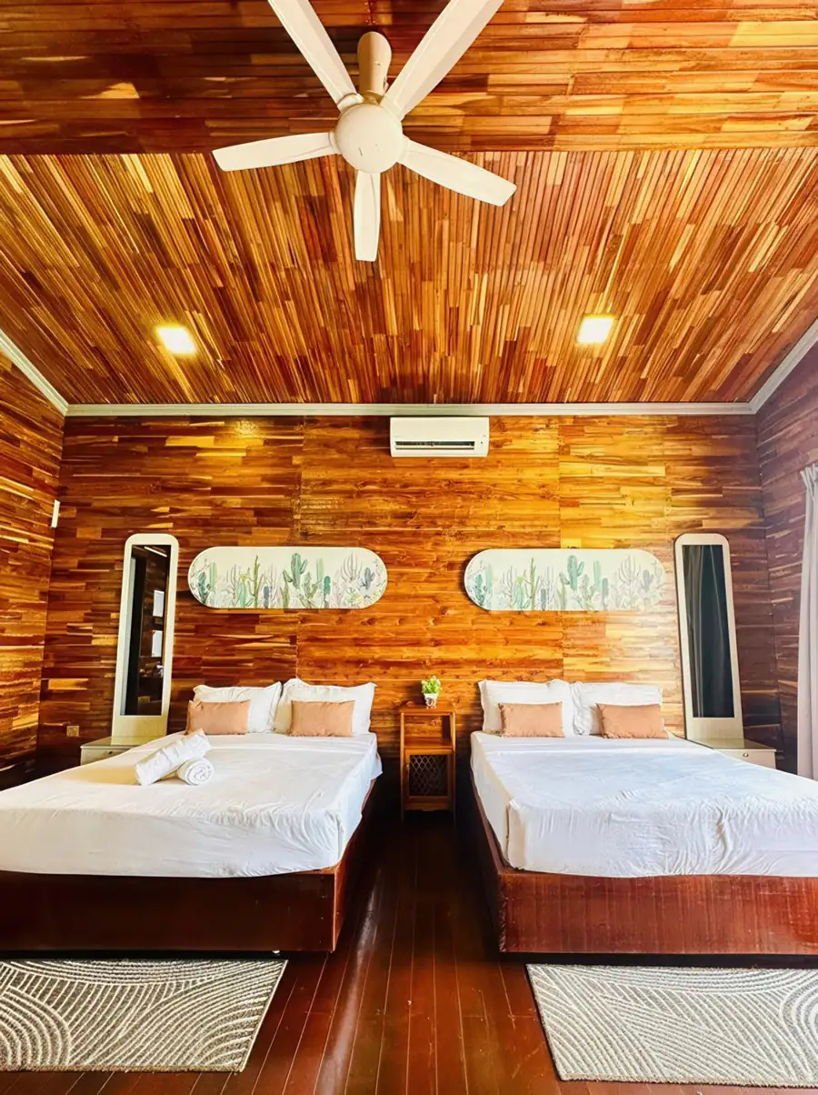 A warm, inviting bedroom at Dayang Resort near the Tun Sakaran Marine Park featuring two large beds, a ceiling fan, traditional style wooden walls with polished timber floors, and AC.