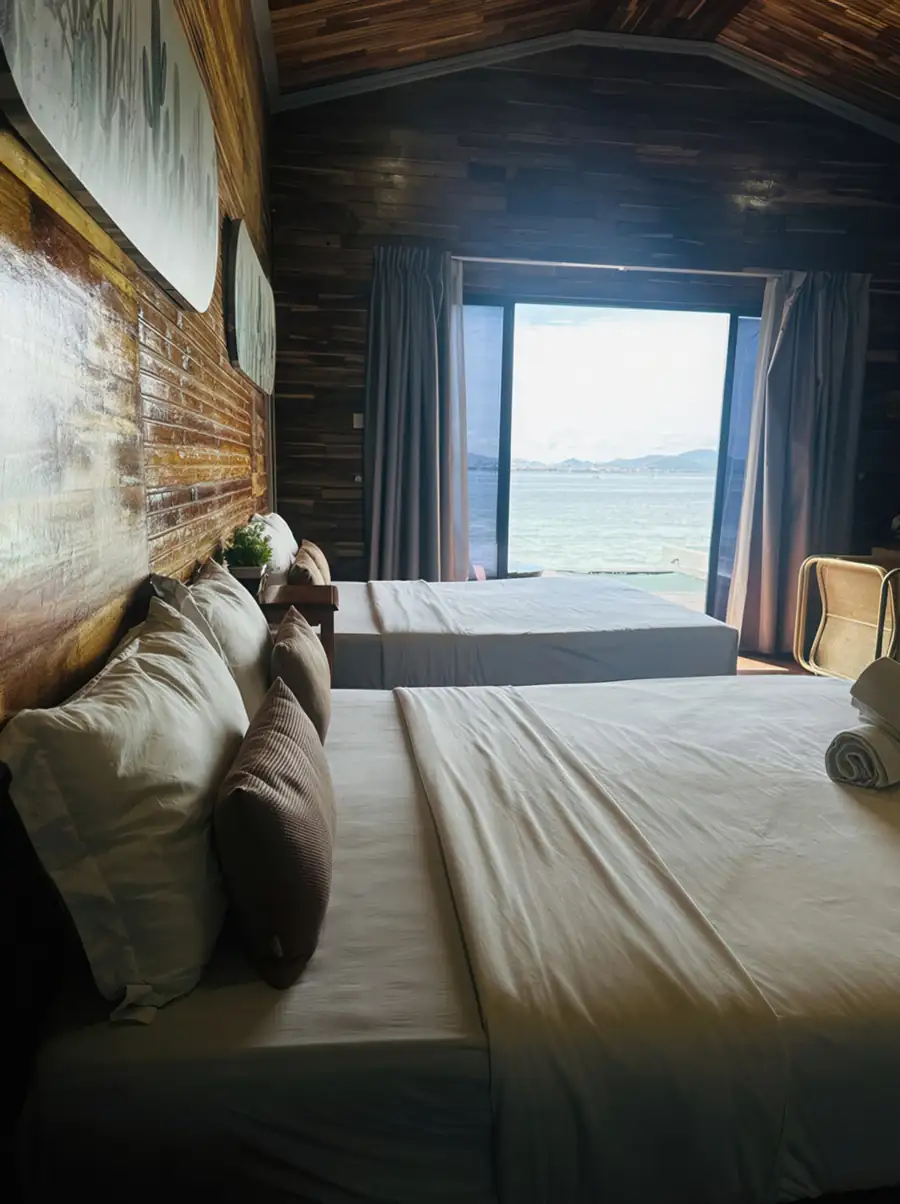 An ocean view bedroom at Dayang Resort on the Celebes Sea featuring two beds, panoramic glass doors framing the seaviews, traditional style wooden walls with polished wood floors, and AC.