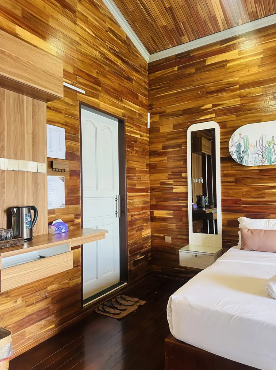 A classic bedroom entrance at Dayang Resort near Pulau Bum Bum featuring a comfortable bed, luggage rack, traditional style wood panel walls with polished teak floors, and A/C.