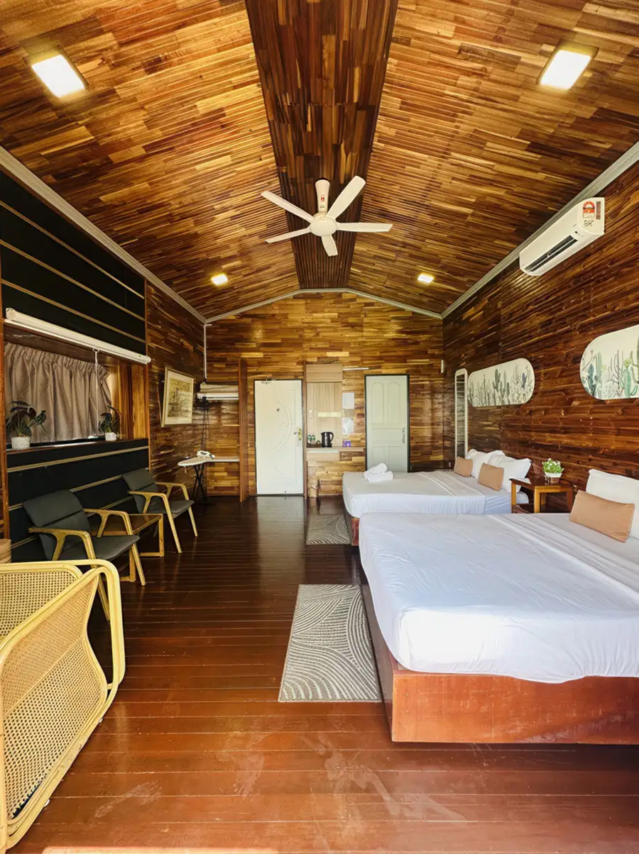 A spacious family bedroom at Dayang Resort in Semporna featuring two large beds, a cozy sitting area, traditional style wood walls with beautiful wooden floors, and air con.