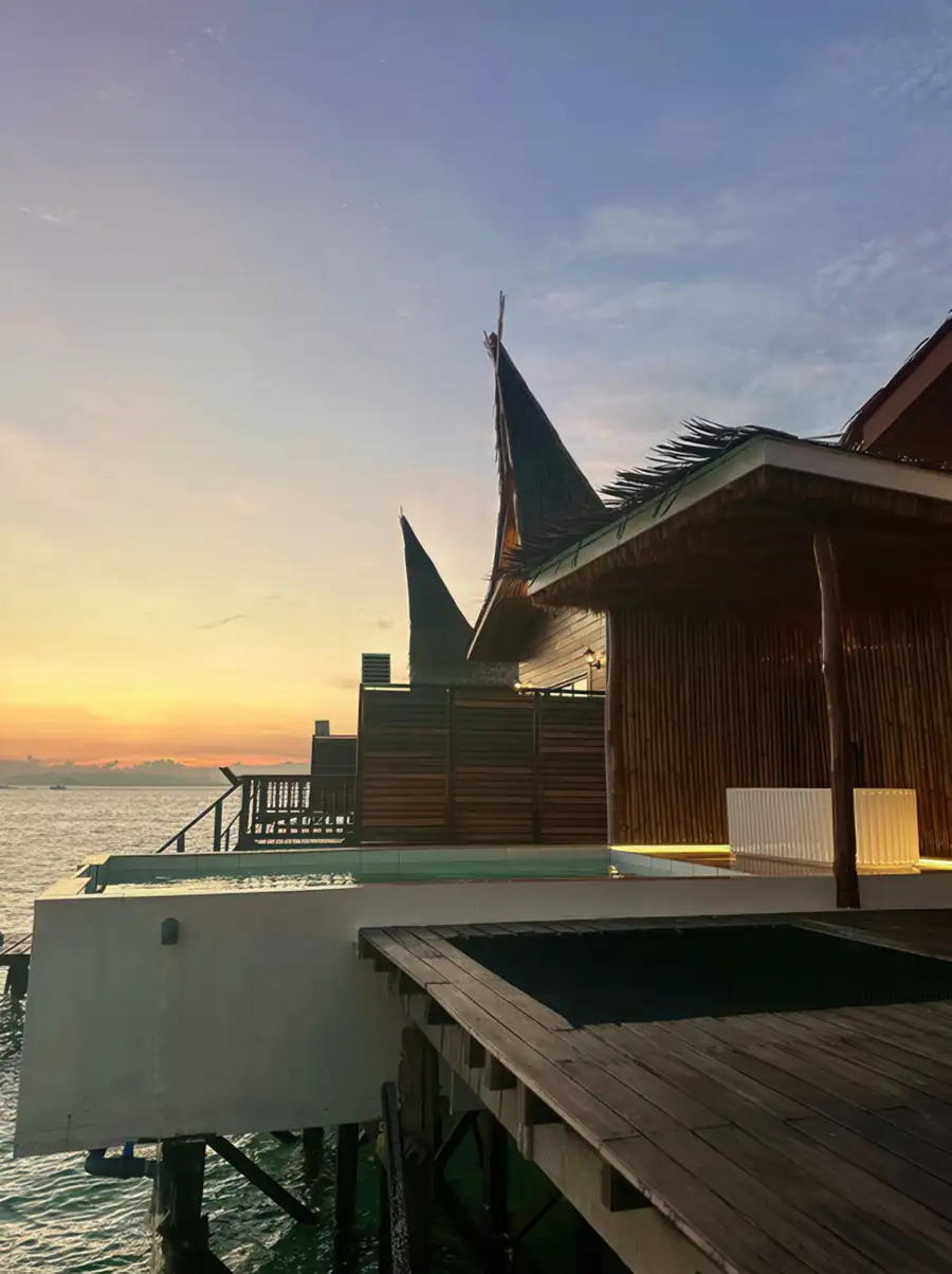 A traditional wooden villa with a distinctive high-pointed roof and a private pool area overlooking the sea at sunset at Dayang Resort.
