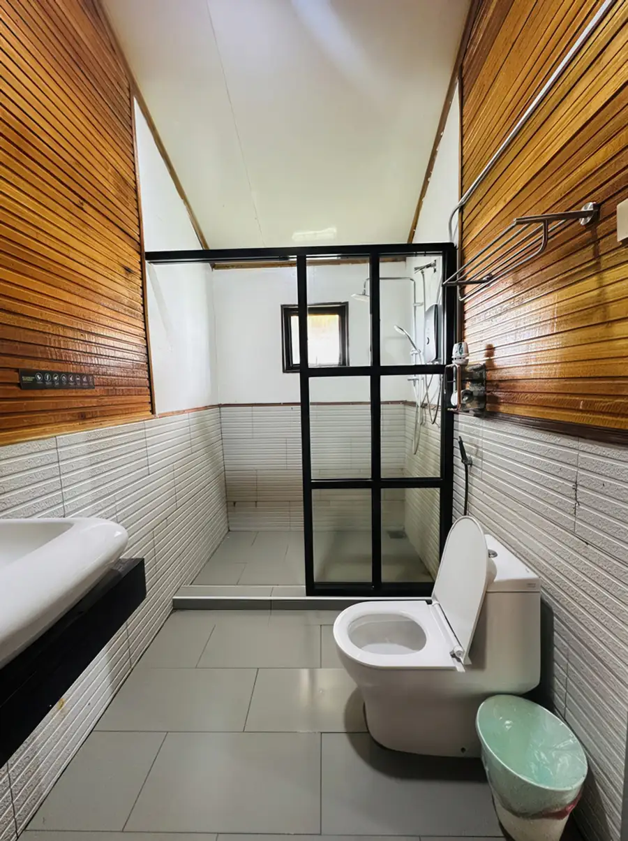 An elegant vanity space inside the bathroom at Dayang Resort showing rich wood-patterned wall tiles, a sleek modern washbasin, a round wall mirror, and convenient bathroom amenities.