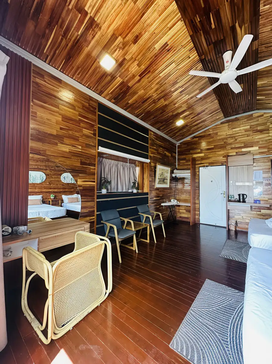 A spacious bedroom seating area at Dayang Resort near Pulau Bum Bum featuring a vanity desk, modern rattan chair, traditional style wooden walls with glossy timber floors, and AC.